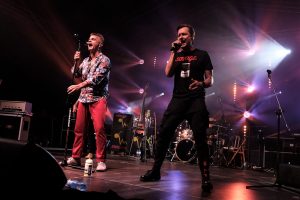 Zdjęcie przedstawia dwóch wokalistów Budki Suflerana śpiewajacych razem na scenie.