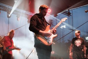 gitarzysta Budki Suflera Piotr Bogutyn gra na gitarze na drugim planie basista Mieczysław Jurecki i wokalistaJacek Kawalec scenie i